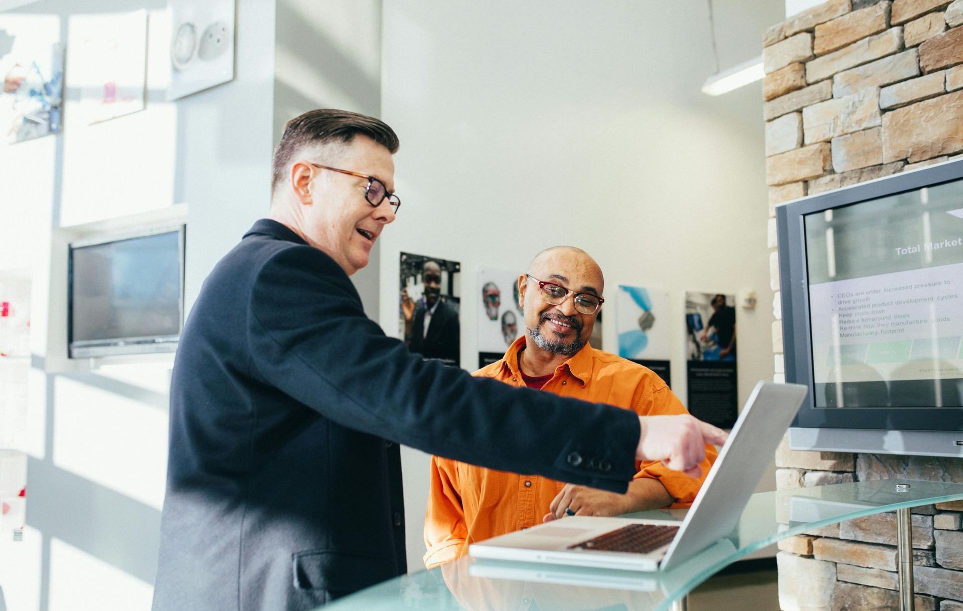 Two men are sitting at a table looking at a laptop computer.