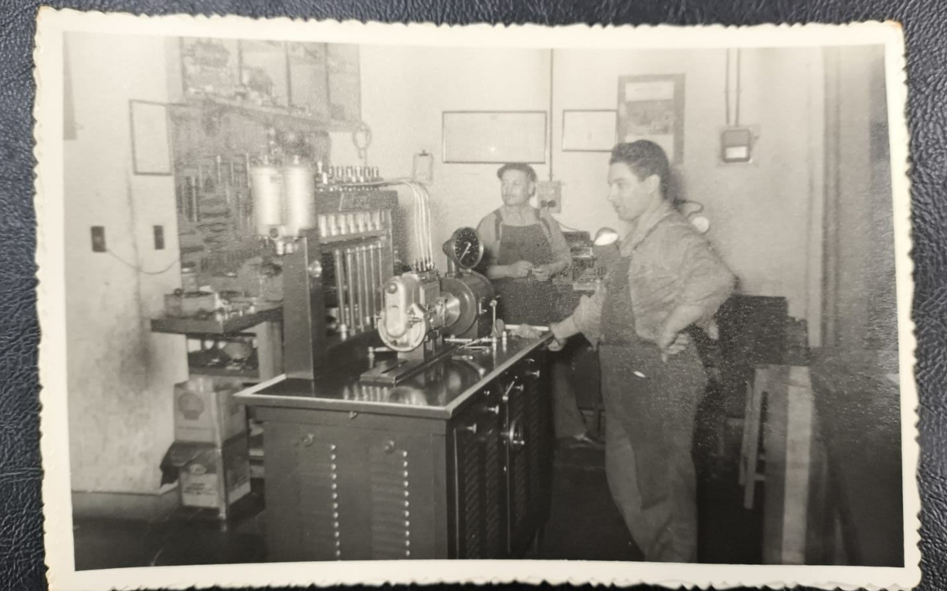Dos hombres con monos de trabajo en un taller, operando maquinaria.