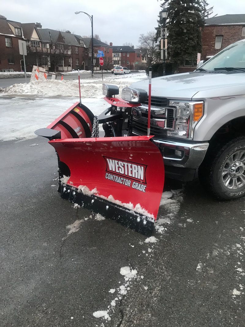 A snowplow on a silver pickup truck clearing a street on a snowy day.