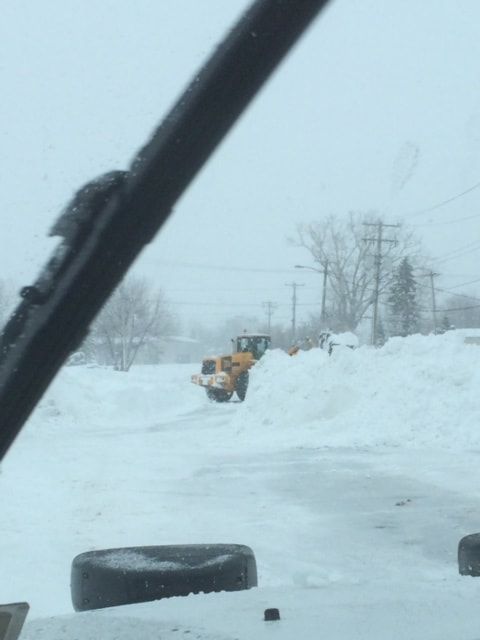 Snowplow clearing a snowy parking lot on an overcast day.