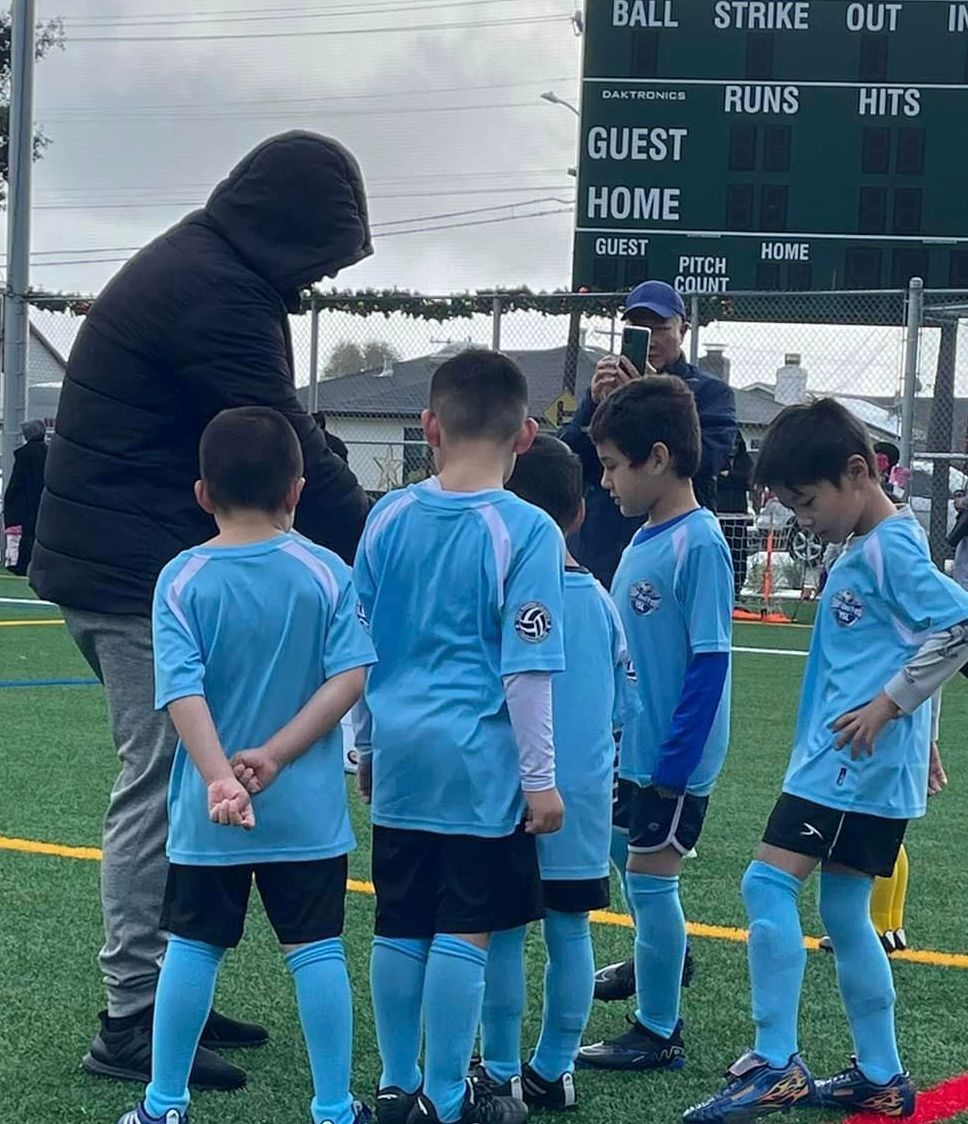 A group of young boys are standing on a soccer field louth their coach looking at a play board.