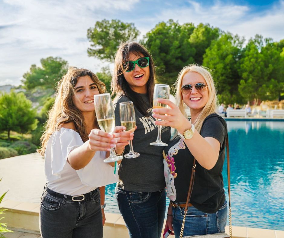 Three women toasting champagne glasses by a pool.