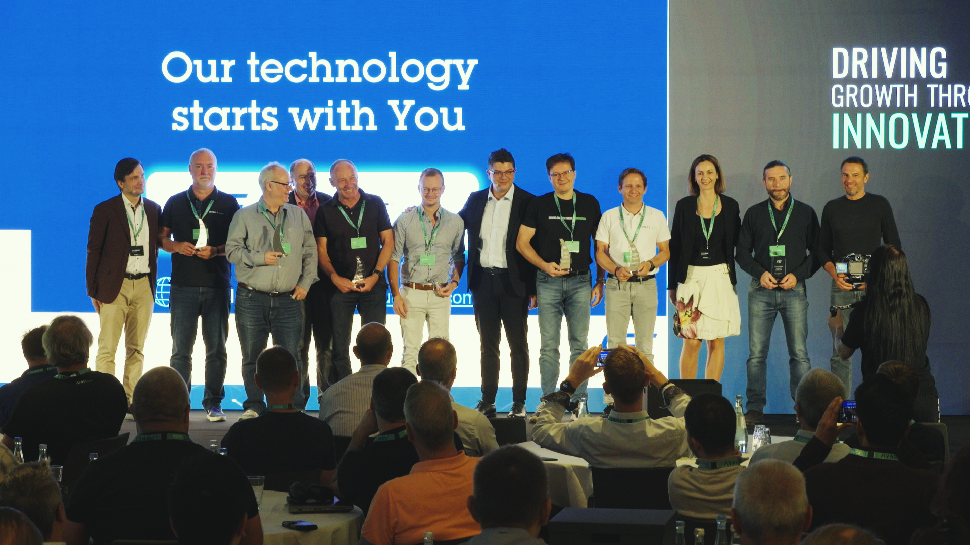 Group of people on stage, holding awards, in front of a screen that says