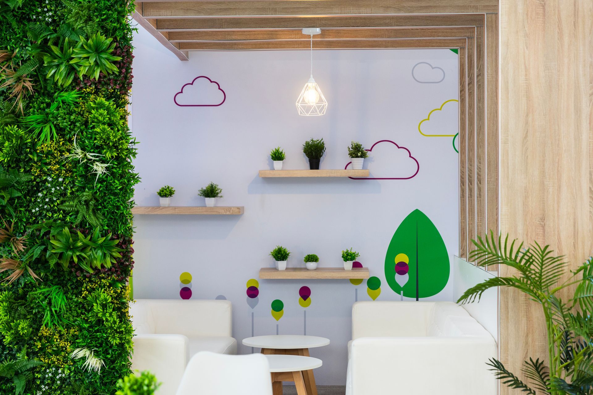 Cozy lounge with white chairs, small round table, shelves with plants, and a wall of green plants.