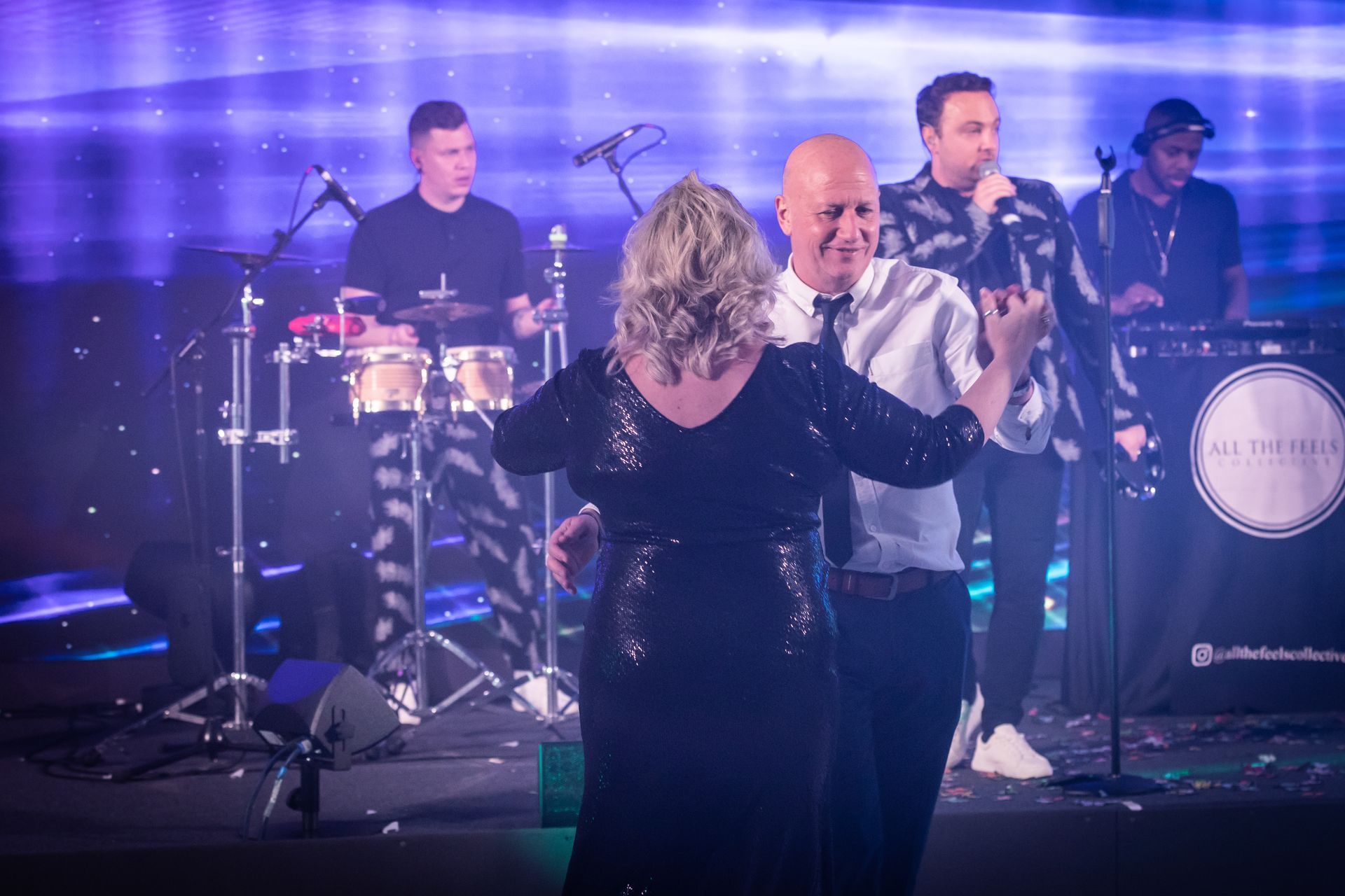 People dancing in front of a band on a stage, with lights and confetti.