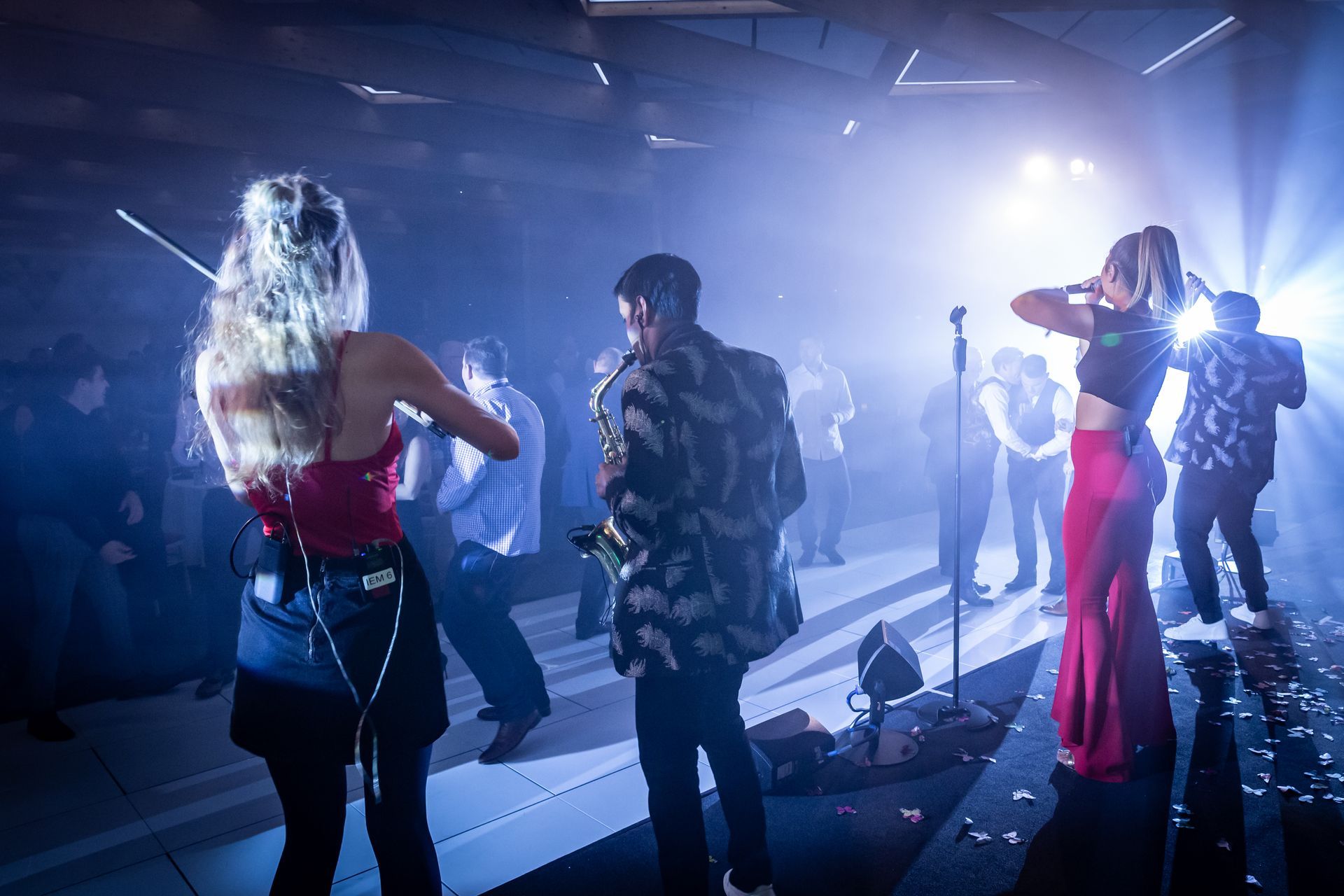 Band performing on stage under blue lights. Violinist, saxophonist, and singer in a dimly lit venue.