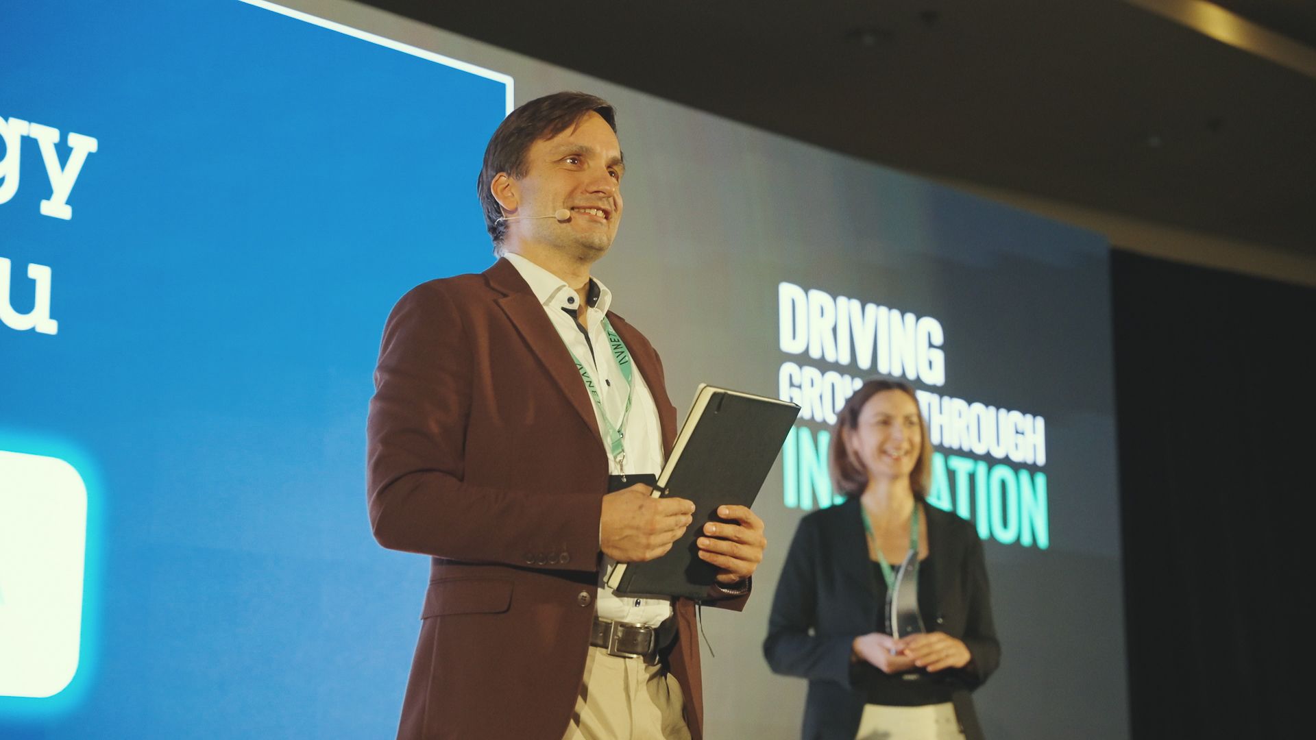 Man in a suit speaks at a conference. A woman stands beside him.