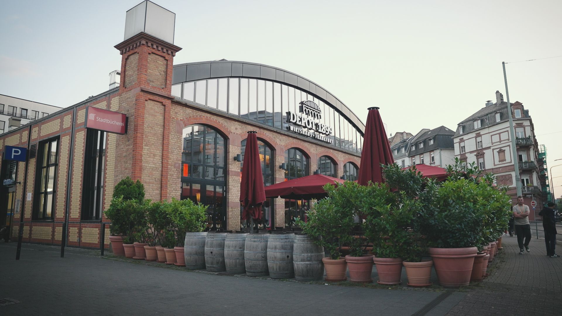 Restaurant with brick exterior, arched windows, outdoor seating, and potted plants on a city street.