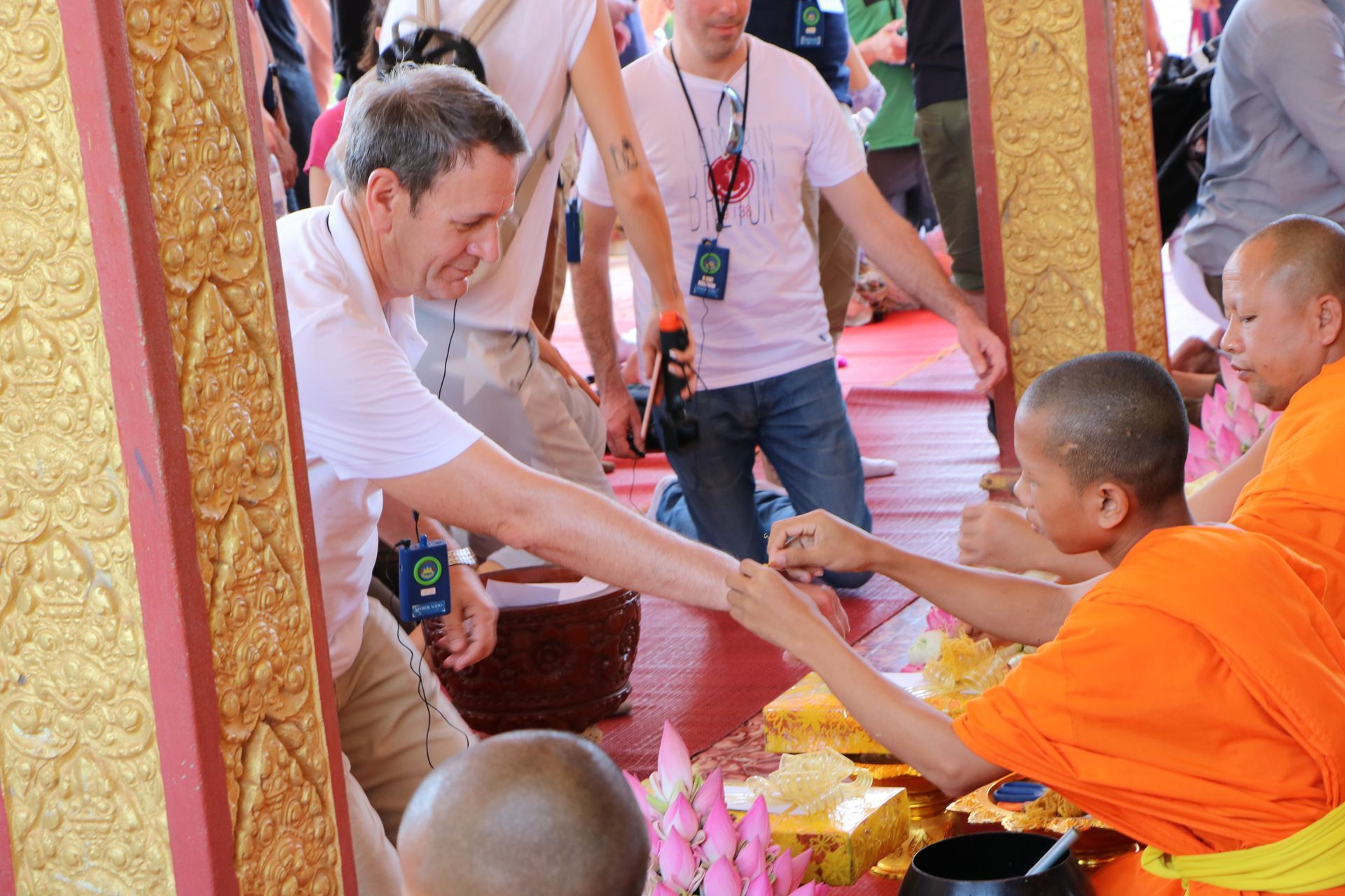 Man in white shirt offering food to Buddhist monks in orange robes, outdoors.