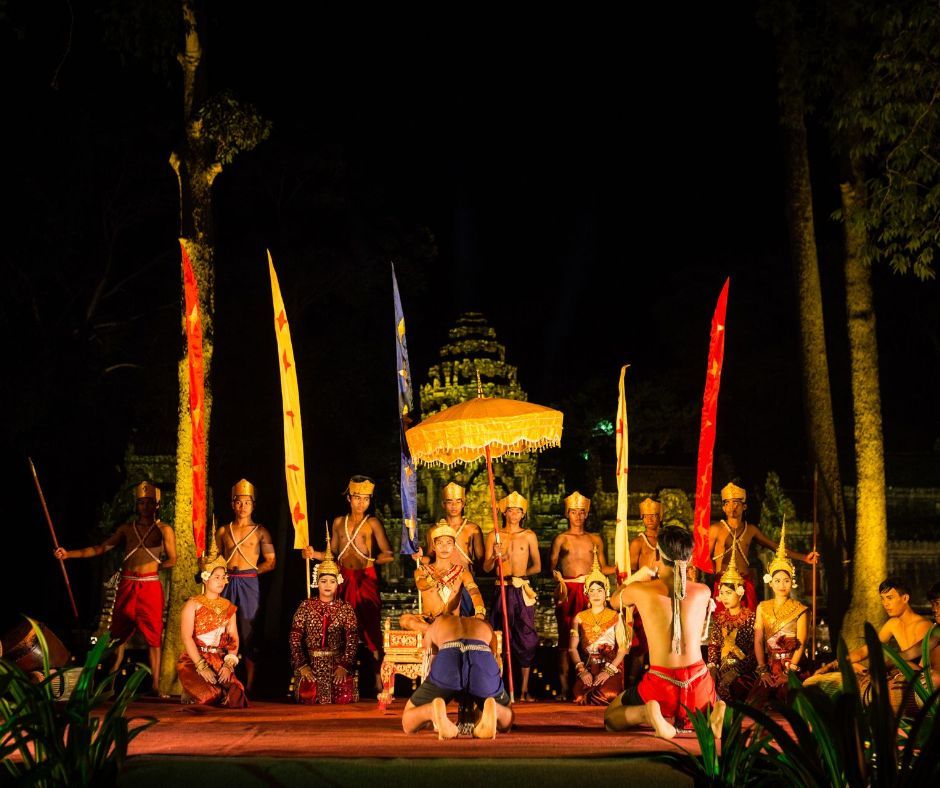 A Cambodian traditional dance performance on a stage at night, with dancers in colorful costumes, against an ancient temple backdrop.