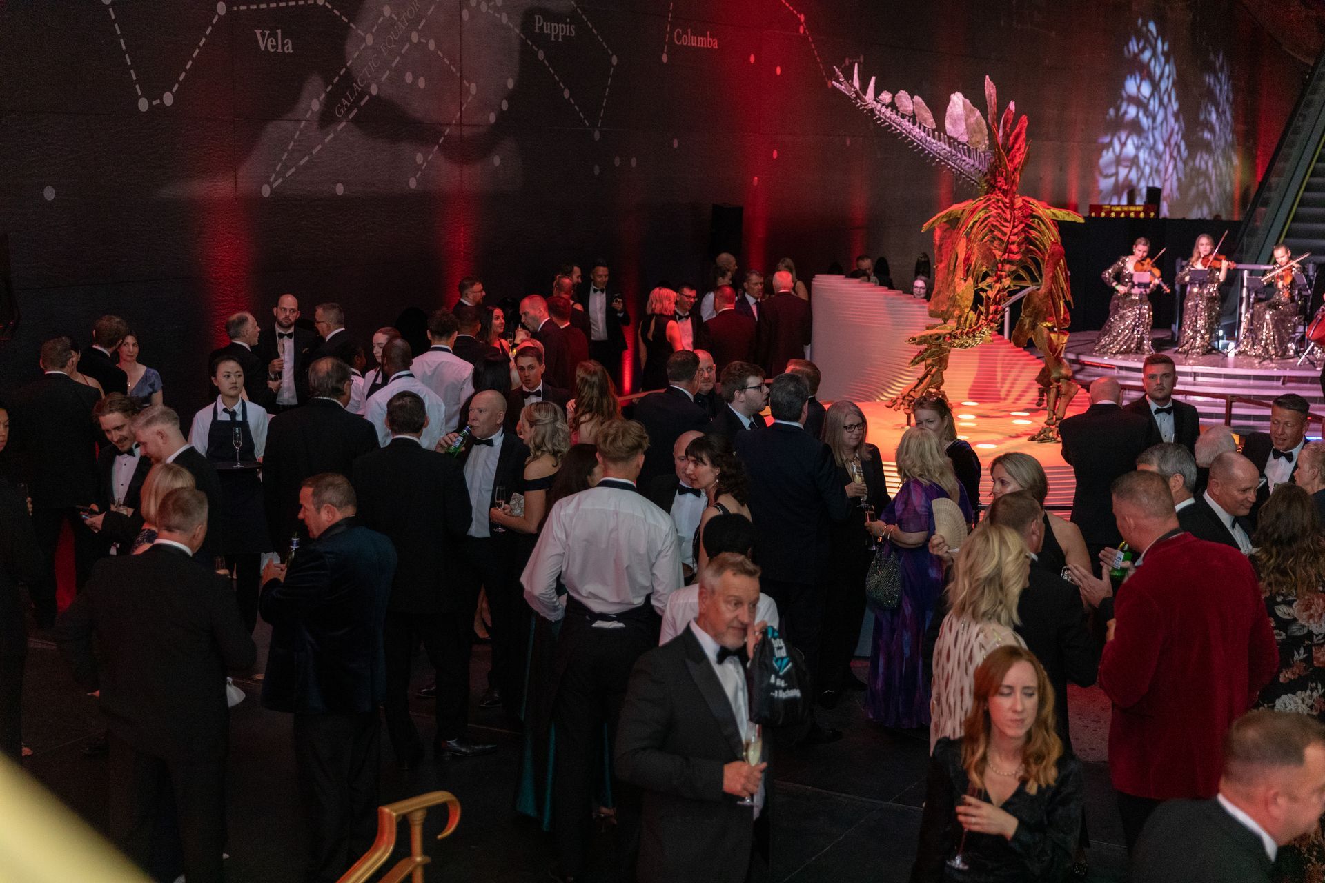 Gala event with people in formal attire, some dancing. Stage with band and a decorative, golden sculpture.