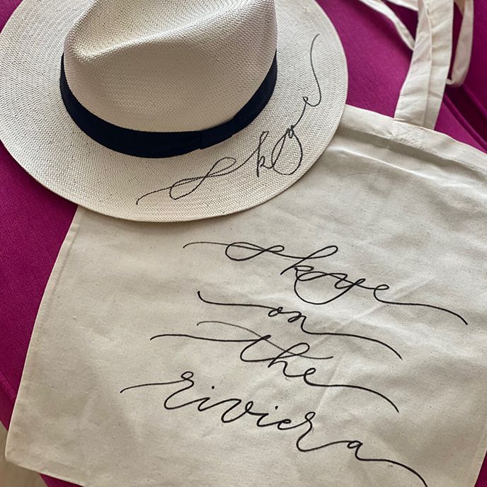 A white hat is sitting next to a white tote bag that says change on the riviera