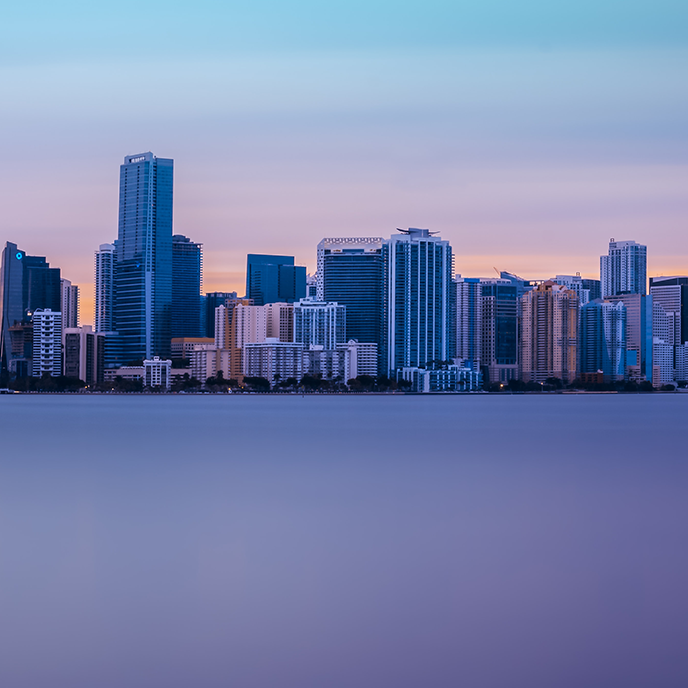 A city skyline overlooking a body of water at sunset.