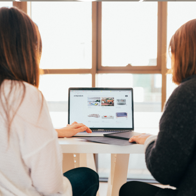 Two women are sitting at a table looking at a laptop