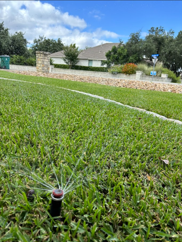 A lawn sprinkler is spraying water on a lush green lawn.