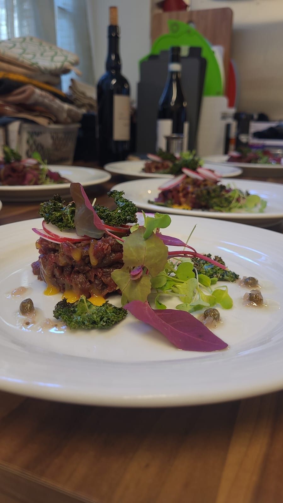 Lautasella tarjoiltu gourmet-annos, jossa tummanpunainen pohja, vihreitä vihanneksia, violetteja yksityiskohtia ja kapriksia valkoisella lautasella.