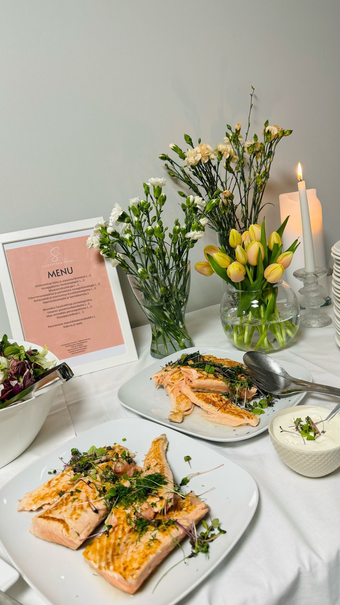 Lohi-illallispöytäkattaus kukilla, salaatilla ja kynttilällä.