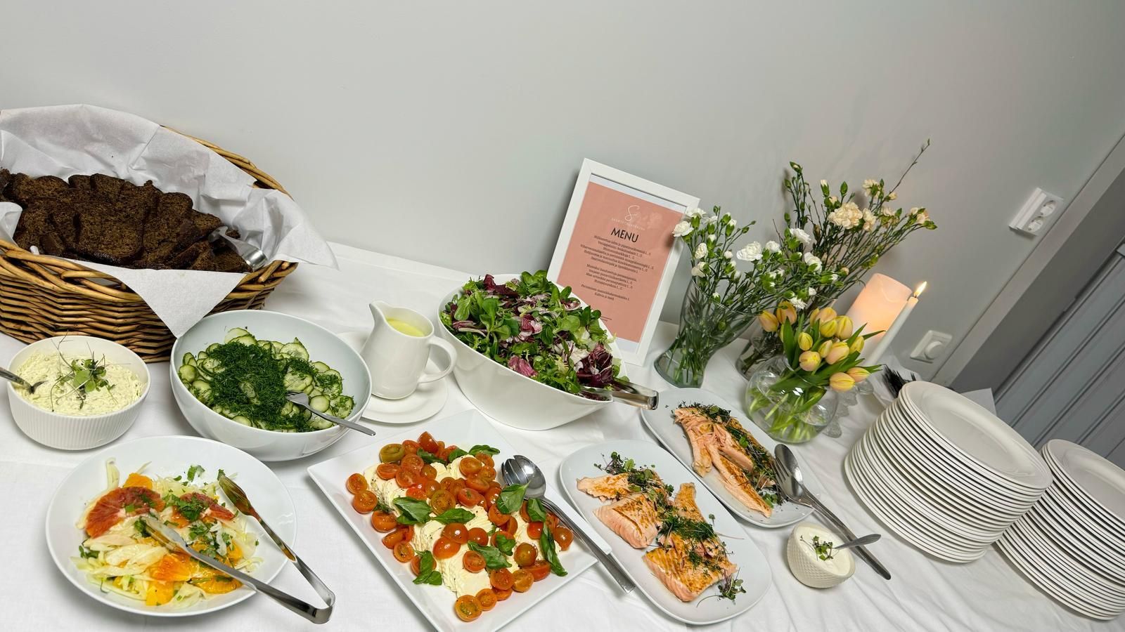 Buffetpöytä, jossa on erilaisia ​​annoksia: leipää, salaattia, tomaatteja, lohta ja kukkia.