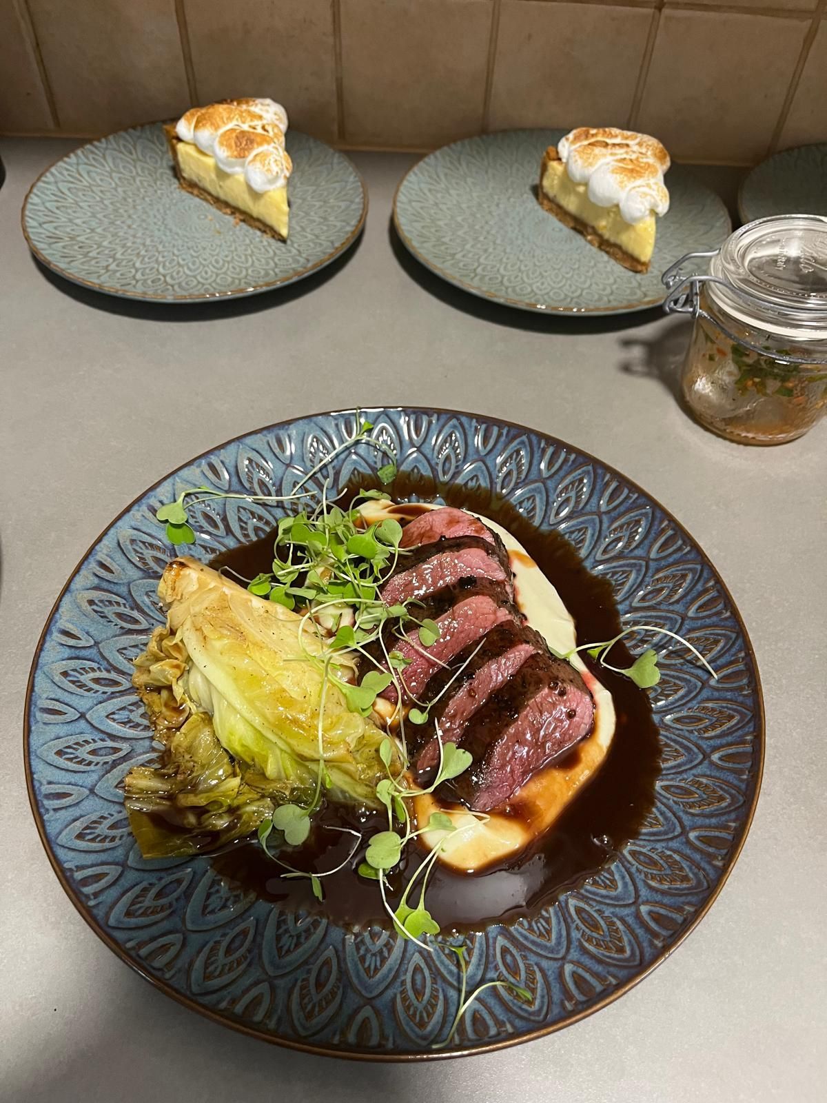 Lautanen, jossa on viipaloitua lihaa, vihreitä ja kastiketta, sekä kaksi sitruunamarenkijälkiruokaa.