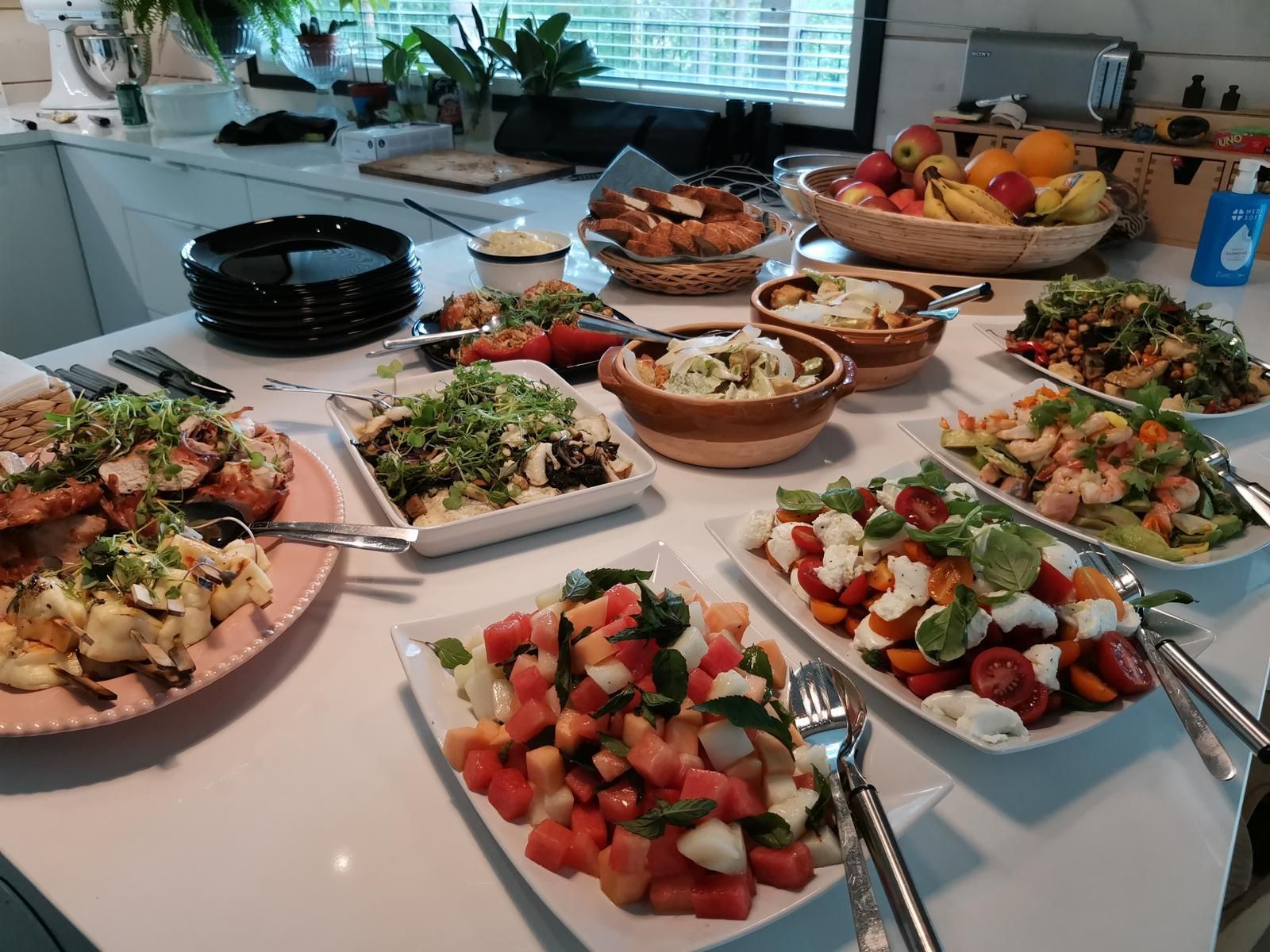 Valkoisella tiskillä on värikkäitä annoksia, kuten salaatteja, hedelmiä ja leipää.