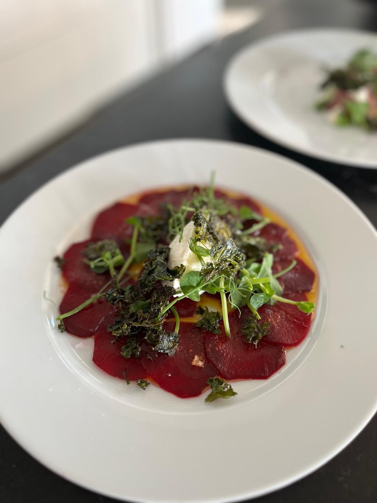 Punajuuricarpaccio vihreiden, juuston ja kastikkeen kera valkoisella lautasella.