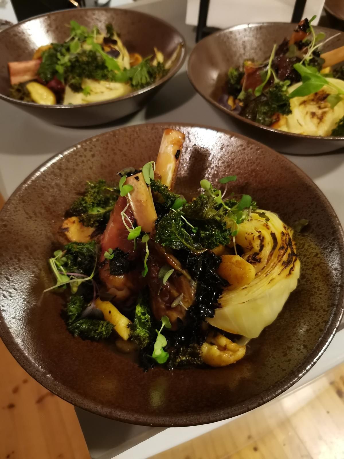 Lautasanko, jossa on grillattuja kasviksia, perunamuusia ja vihreitä ruskeassa kulhossa.