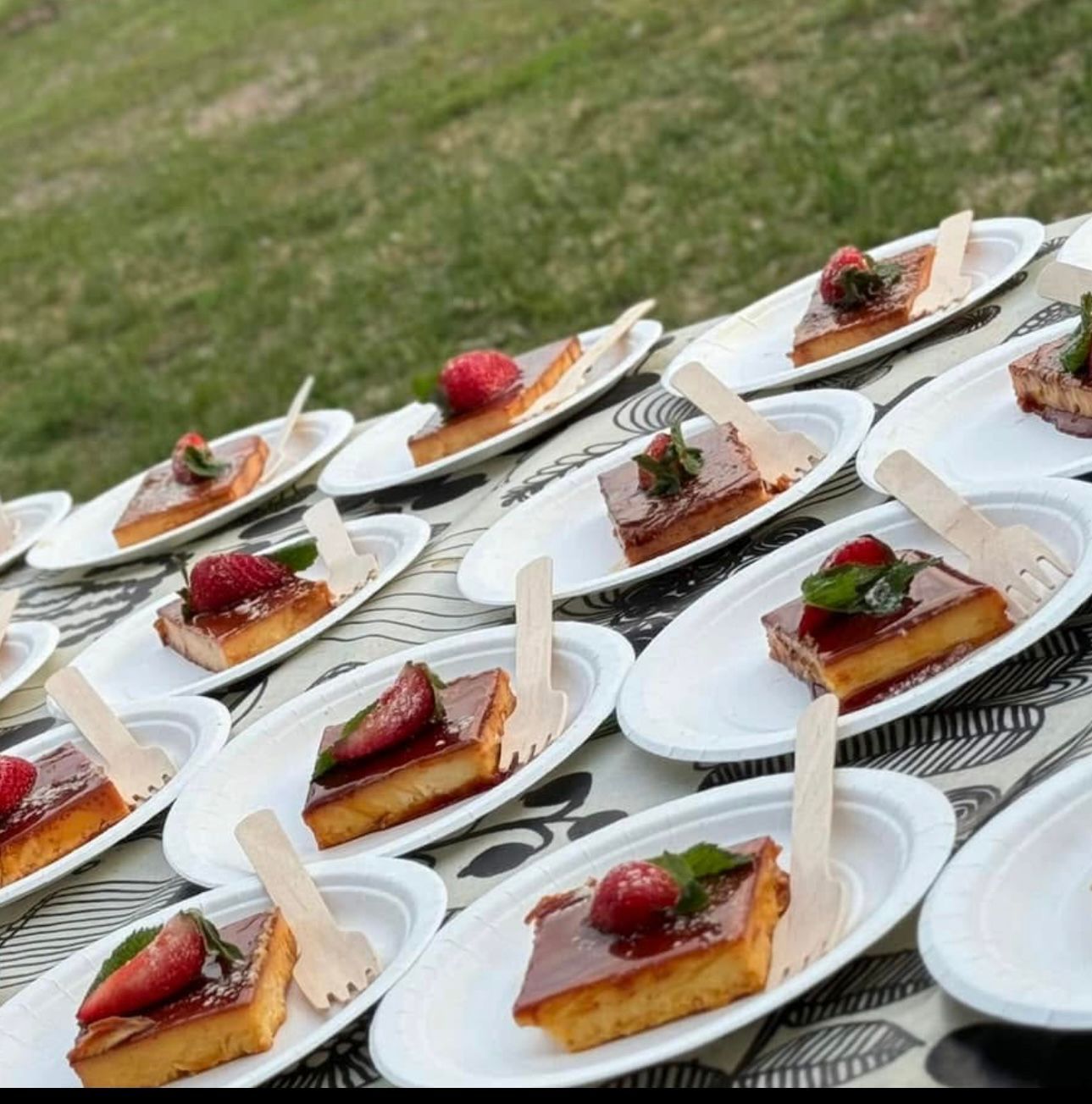 Mansikoilla ja mintulla kuorrutettuja jälkiruokaneliölautasia aseteltuna ulkona pöydälle puisilla haarukoilla.