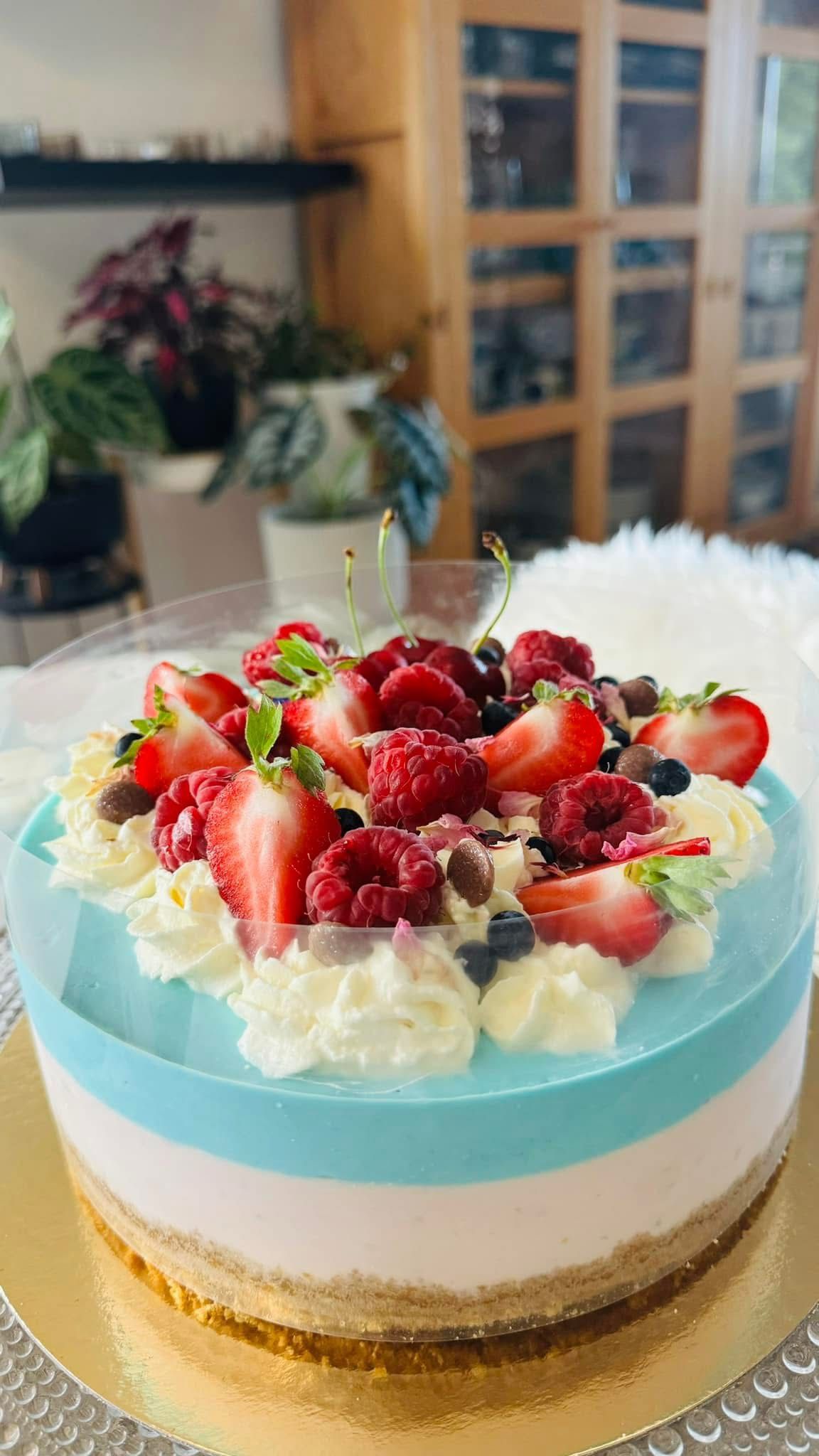 Juustokakku, jossa on sinisiä ja valkoisia kerroksia, päällä kermavaahtoa, marjoja ja suklaahippuja.