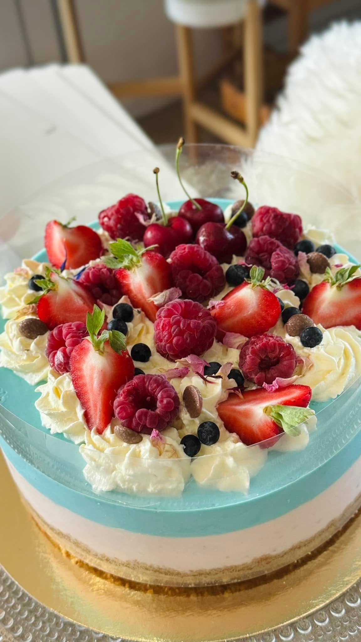 Kakku, jonka päällä on mansikoita, vadelmia ja kirsikoita, sinisiä ja vaaleanpunaisia kerroksia ja kermavaahtoa.
