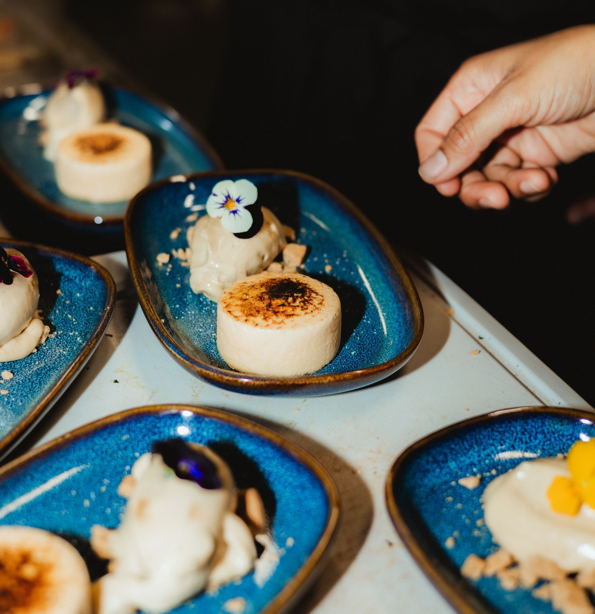 Jälkiruokia sinisillä lautasilla, joissakin karamellisoitu pinta. Käsi ojentaa yhtä.