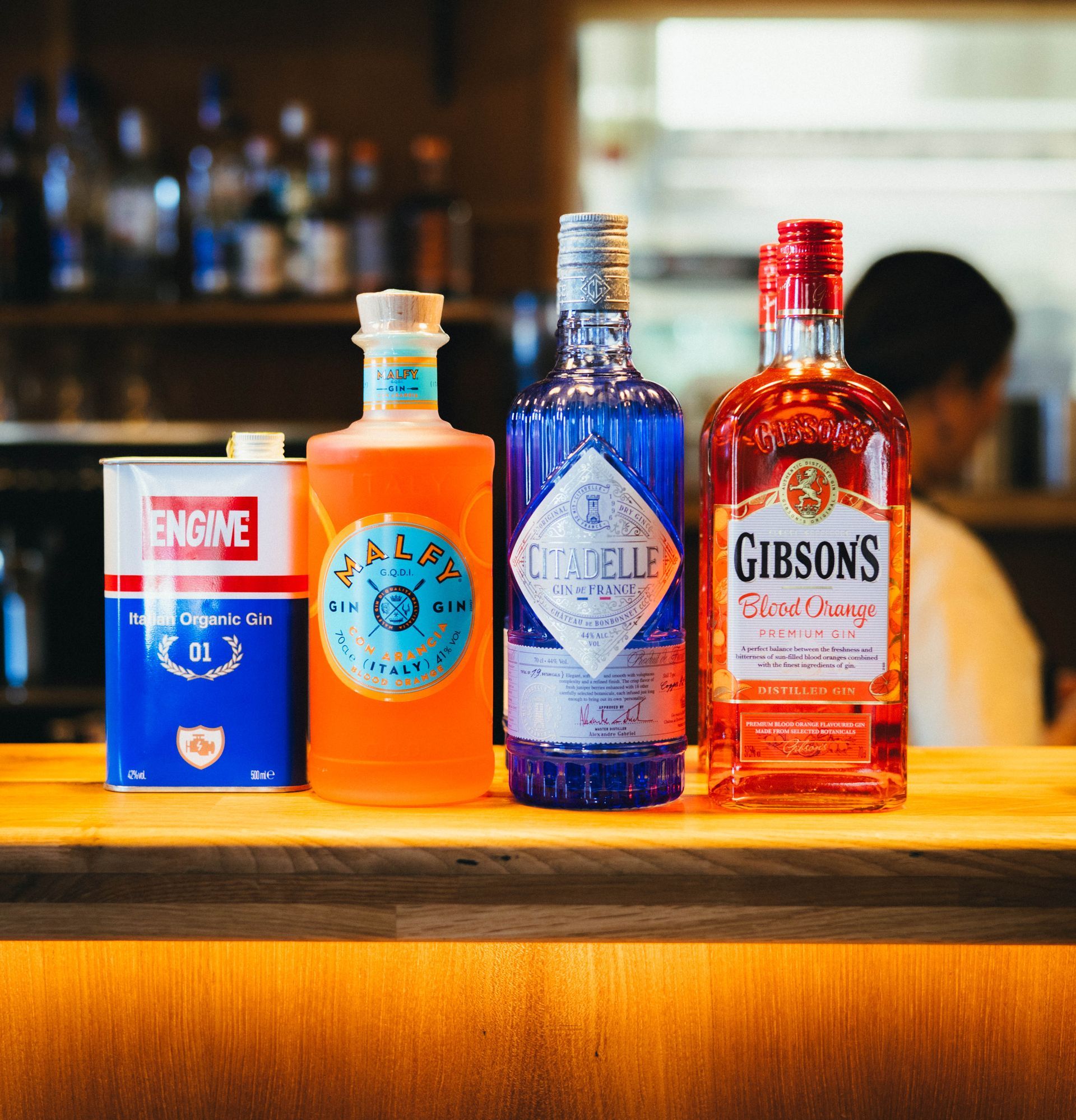 Neljä ginipulloa puisella baaritiskillä: Engine, Malfy, Ondine ja Gibson's Blood Orange. Baarin tausta.