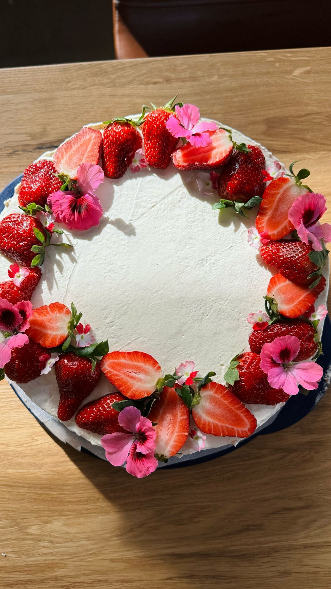 Kakku koristeltuna tuoreilla mansikoilla ja vaaleanpunaisilla kukilla.