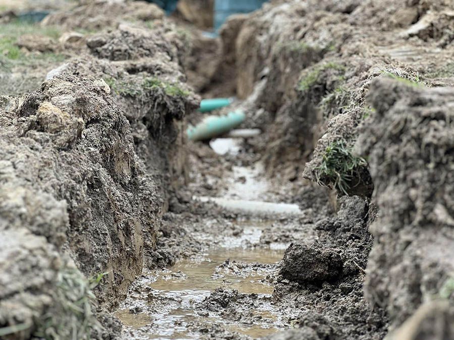 A muddy trench with pipes coming out of it.