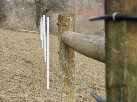 A wooden fence with barbed wire surrounding a field.