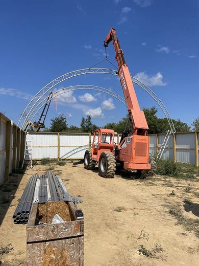 A crane is lifting a metal structure in a dirt field.