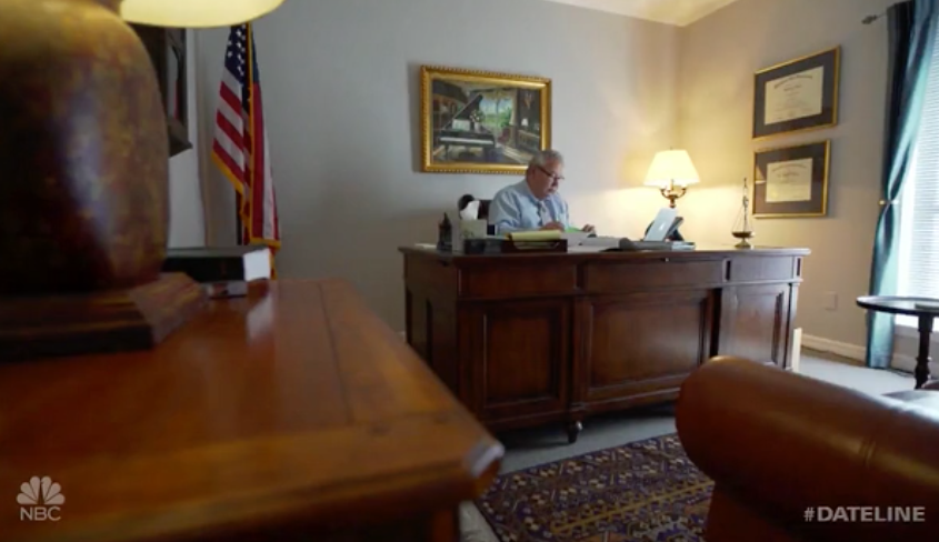 A man is sitting at a desk in a living room.