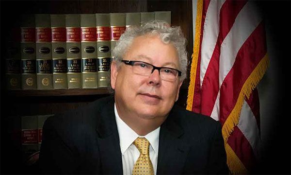 A man in a suit and tie is sitting in front of an american flag.