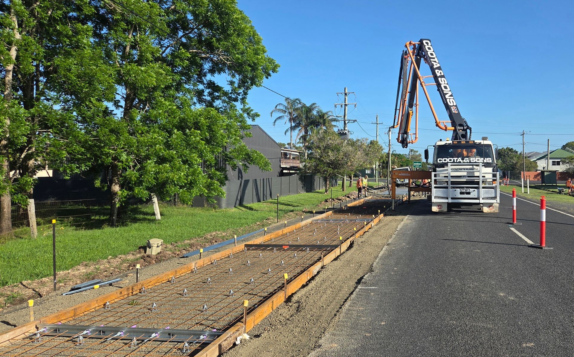 Concrete truck pouring concrete on a road. Roadwork with wooden forms and metal reinforcement. Blue sky.