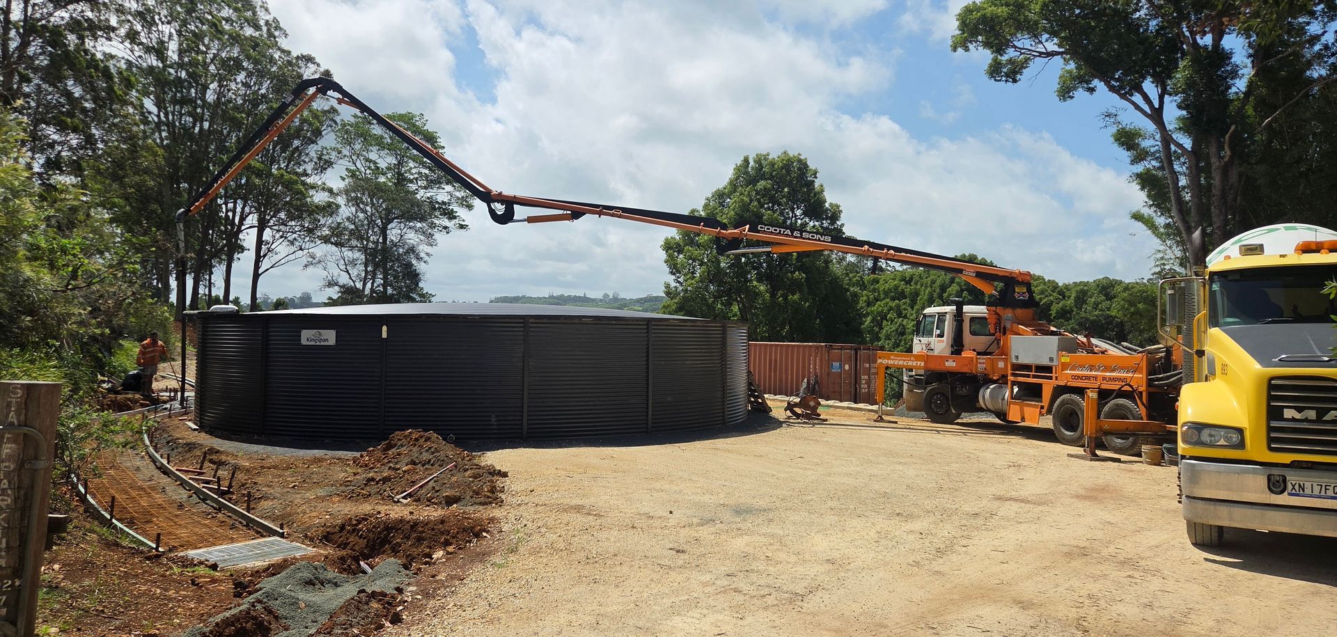 Construction site with concrete pump truck pouring concrete into a large, round tank.