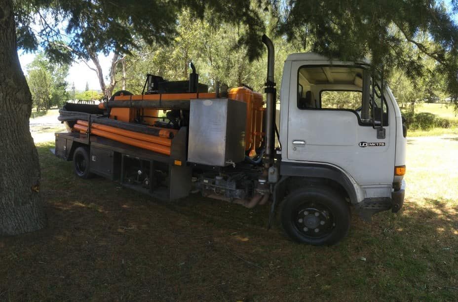 White Truck With Drilling Equipment Parked Under Trees on Grass — Coota & Son's Concrete Pumping In Woodenbong, NSW