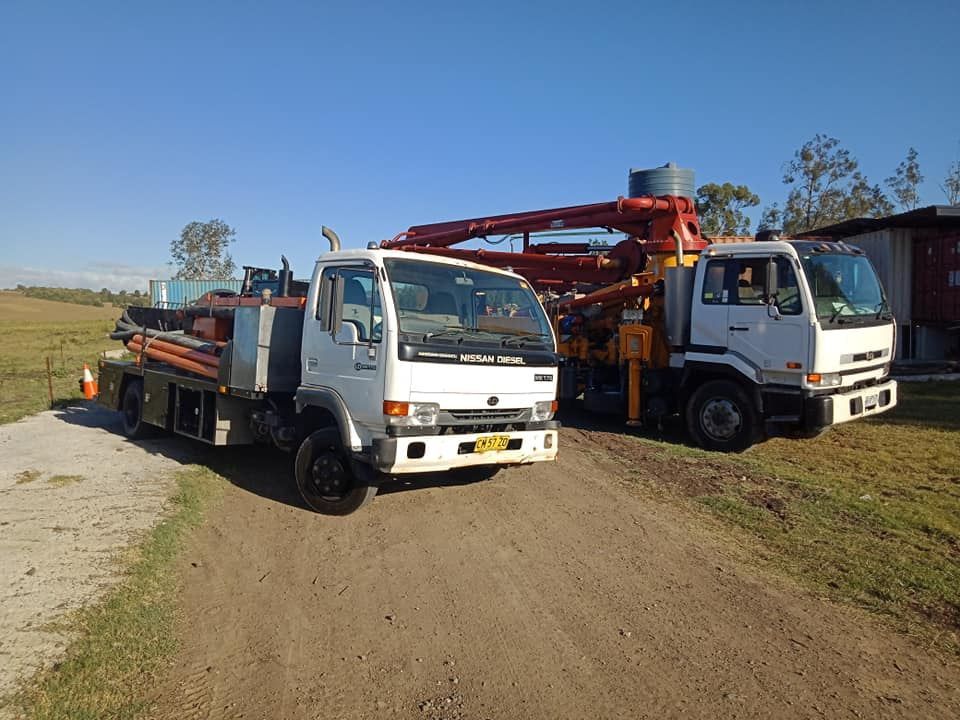 Two White Work Trucks on a Dirt Road in a Rural Setting With Blue Sky — Coota & Son's Concrete Pumping In Maclean, NSW