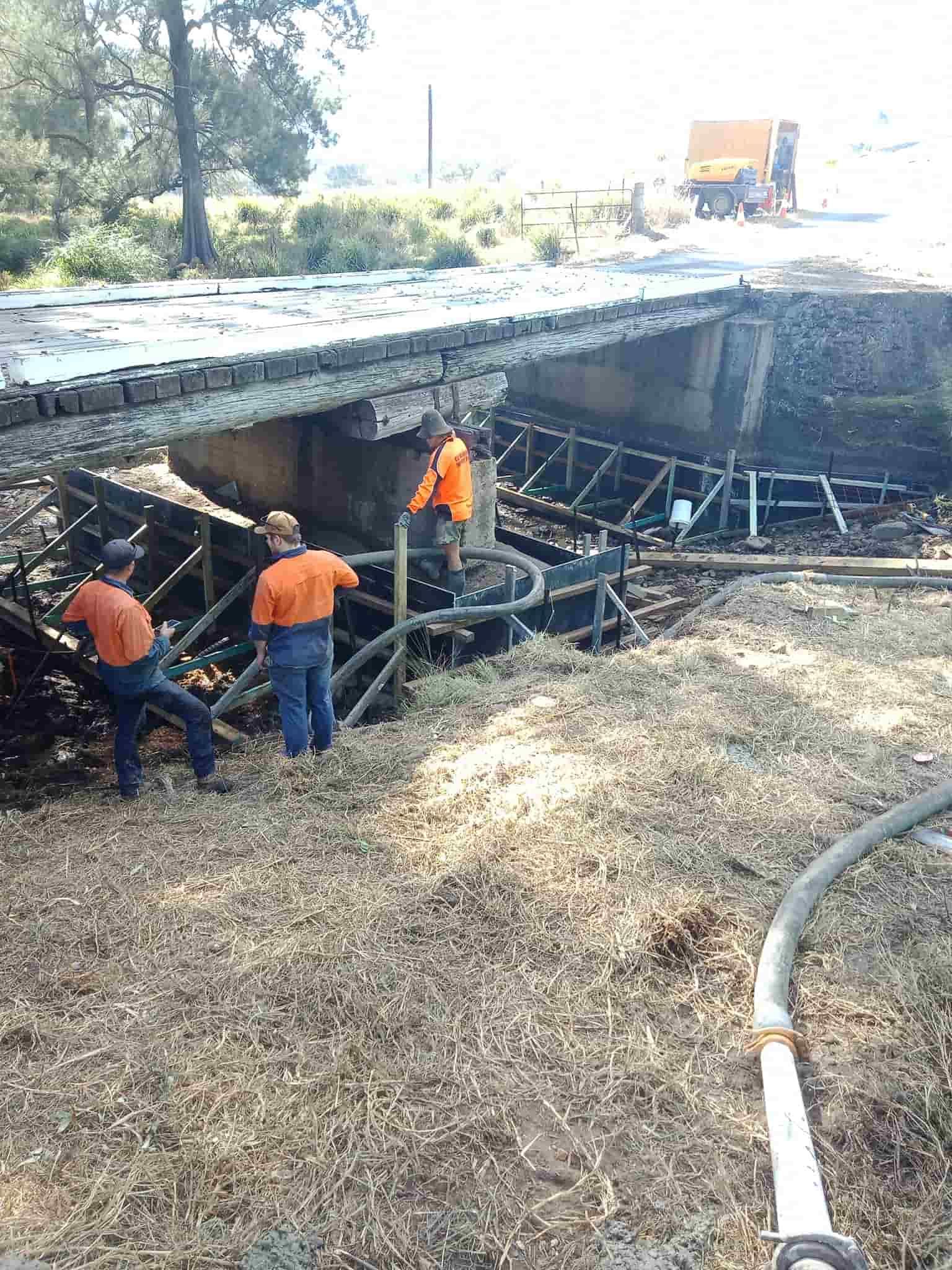 Men in Orange Shirts Examine Damaged Bridge Over a Creek — Coota & Son's Concrete Pumping In South Gundurimba, NSW