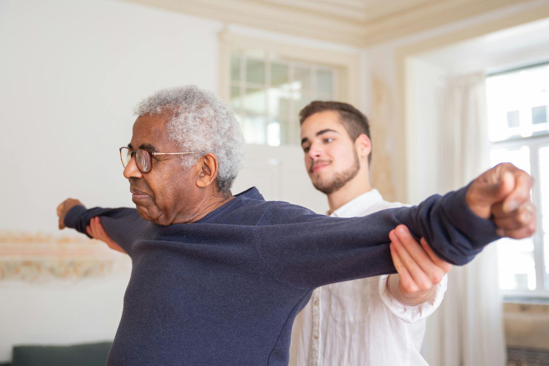 A young man is helping an older man stretch his arms.