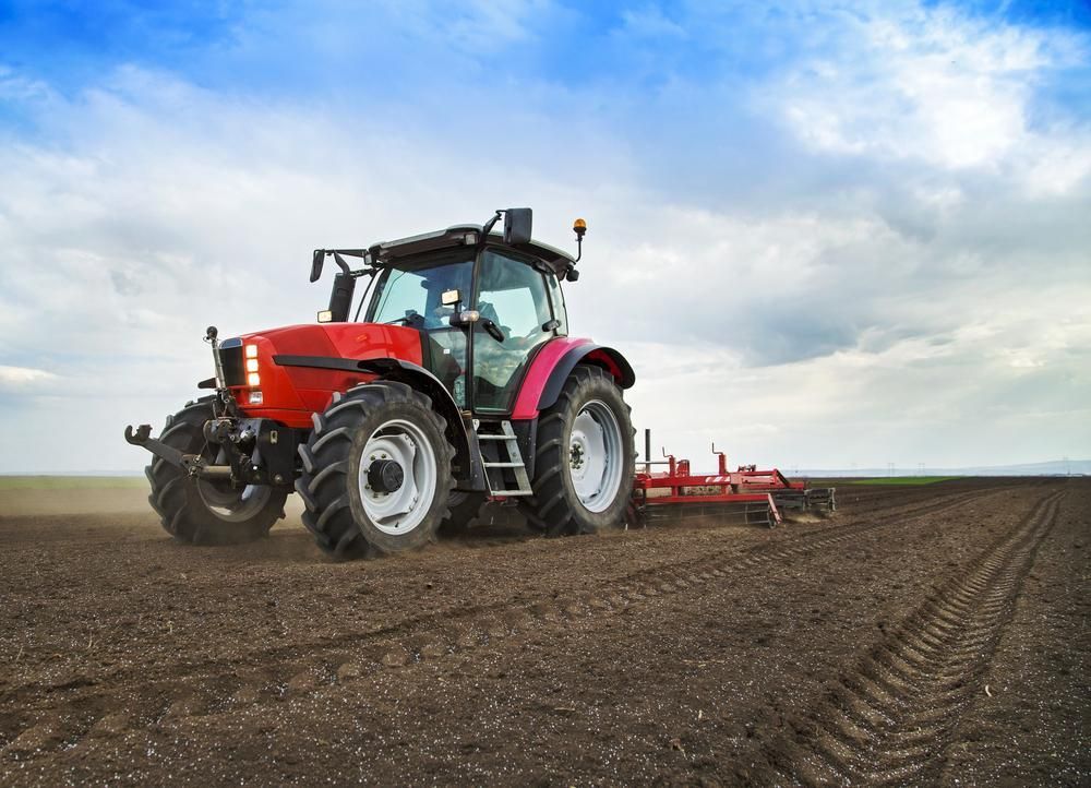 A Red Tractor Is Plowing A Field With A Plow — JBS Mobile In Alstonville, NSW