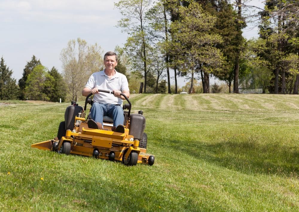 A Man Is Riding A Lawn Mower On A Lush Green Field — JBS Mobile In Richmond Hill, NSW