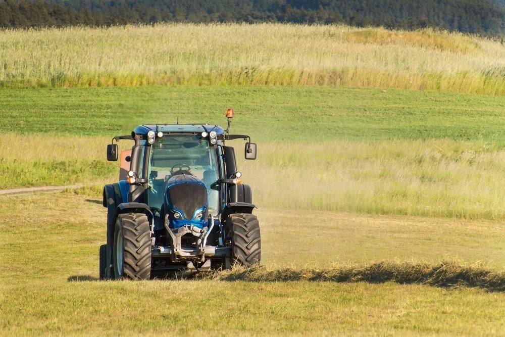A Blue Tractor Is Driving Through A Grassy Field — JBS Mobile In Lennox Head, NSW