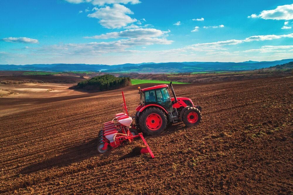 An Aerial View Of A Red Tractor Plowing A Field — JBS Mobile In Richmond Hill, NSW