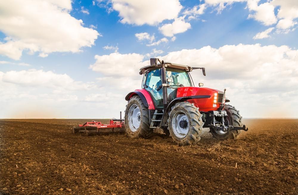 A Red Tractor Is Plowing A Field With A Plow — JBS Mobile In Richmond Hill, NSW