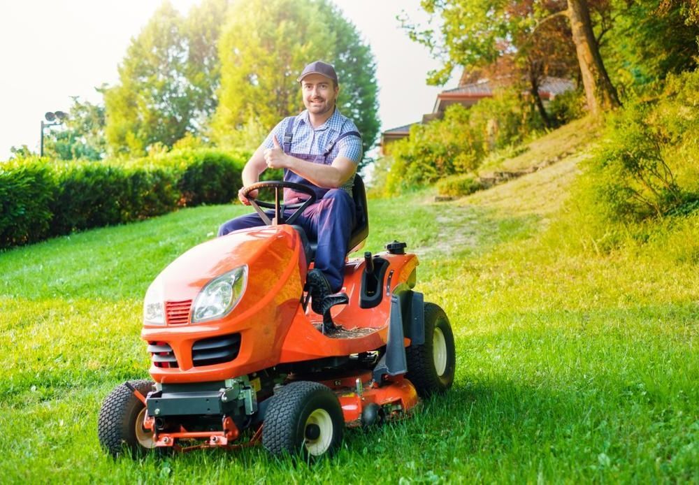 A Man Is Riding A Lawn Mower On A Lush Green Lawn — JBS Mobile In Lennox Head, NSW