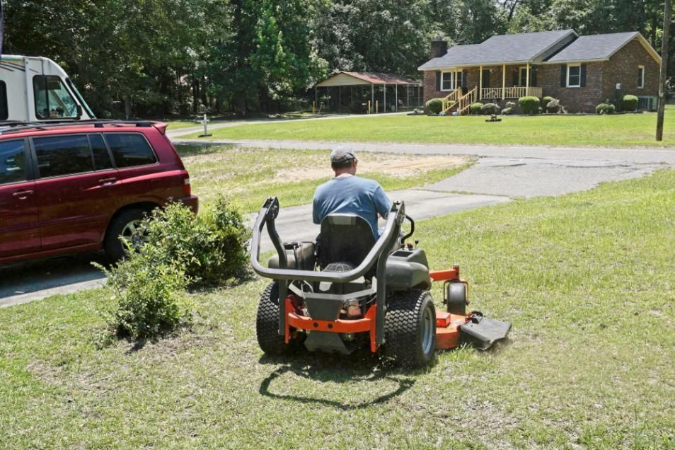 A Man Is Riding A Lawn Mower In Front Of A House — JBS Mobile In Lennox Head, NSW